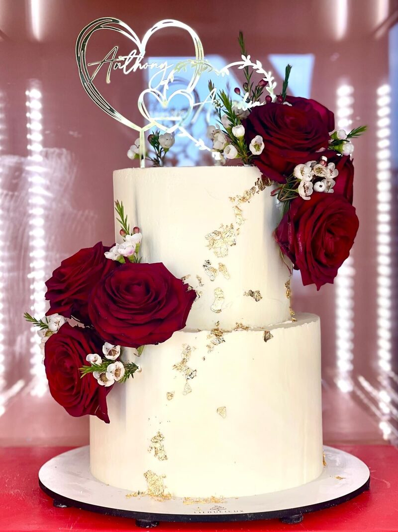 Wedding cake blanc à deux étages, roses rouges et feuilles d'or
